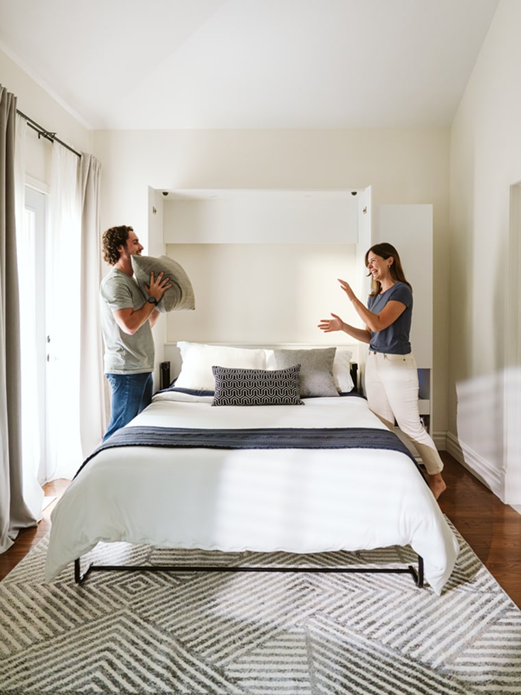 Two people in a bedroom with a Murphy bed.
