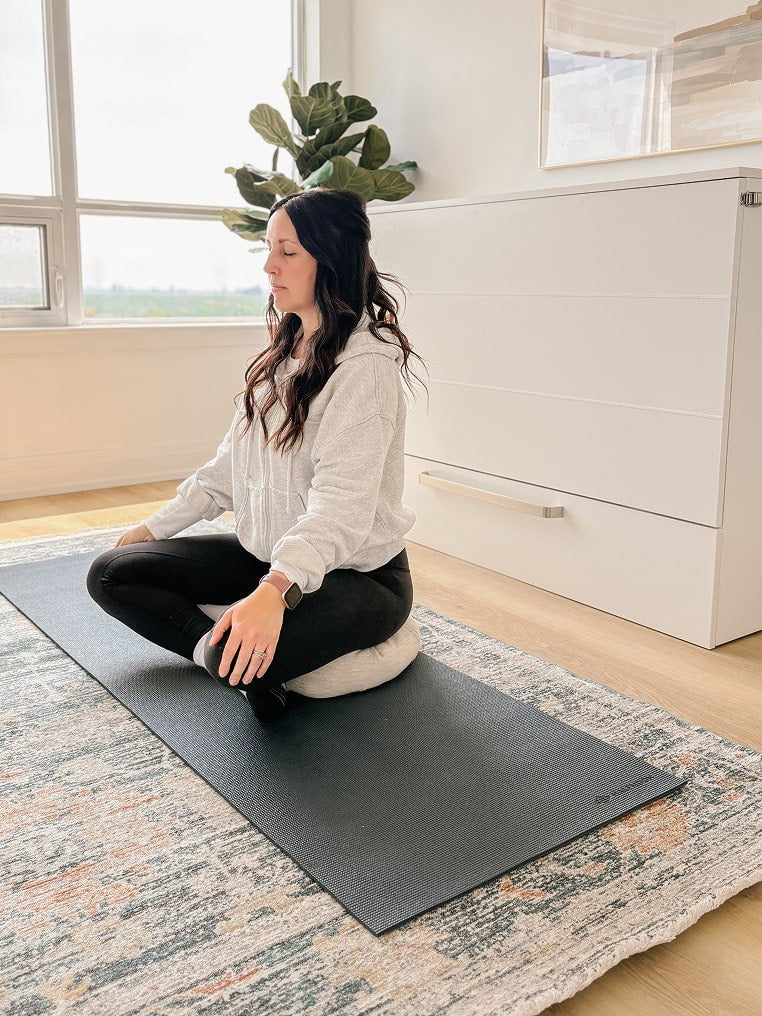 Woman sitting on a yoga mat in a room with a plant and Borealis collection white cabinet bed