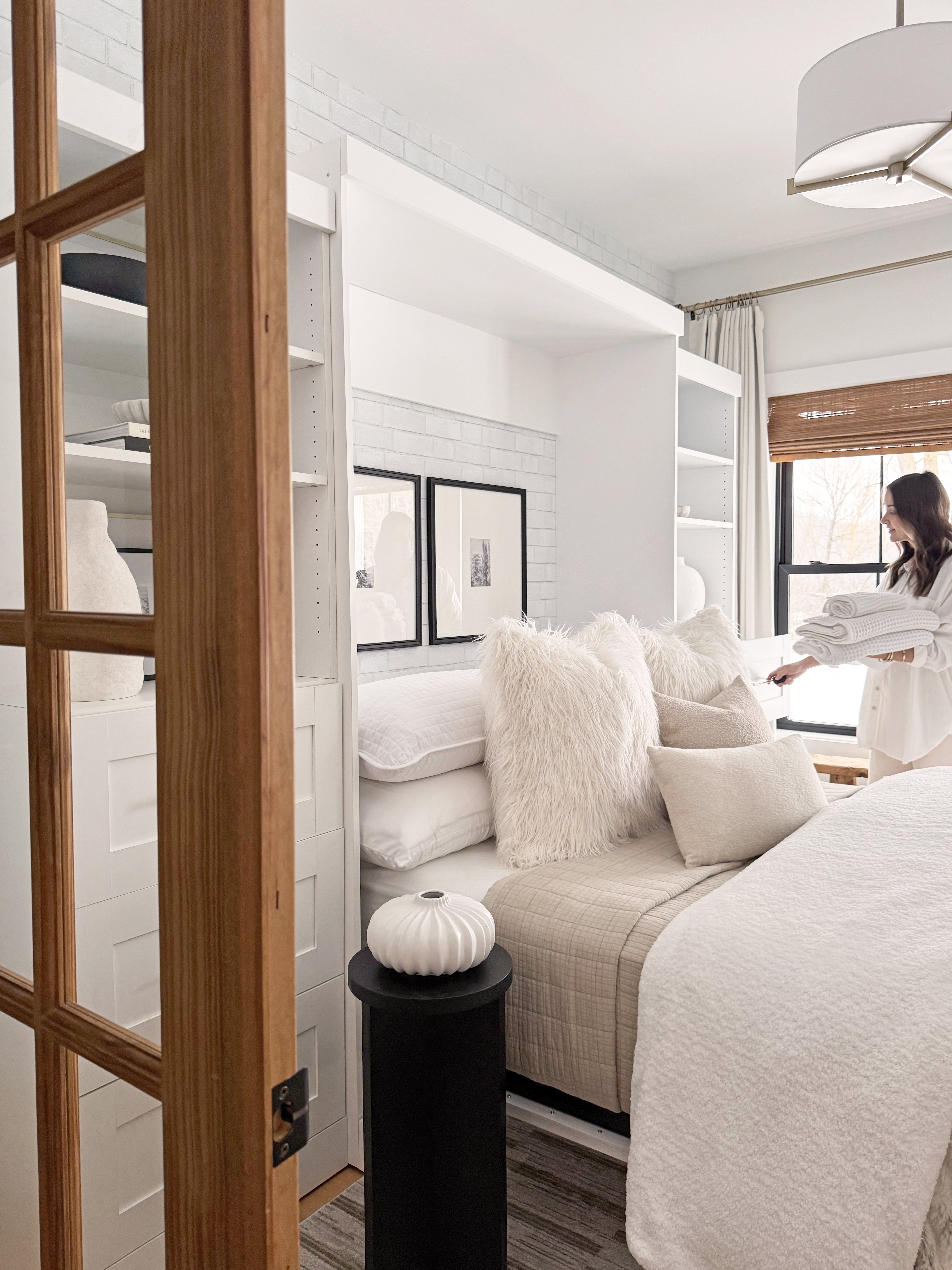 Modern bedroom with a bed, pillows, and a person in the background.