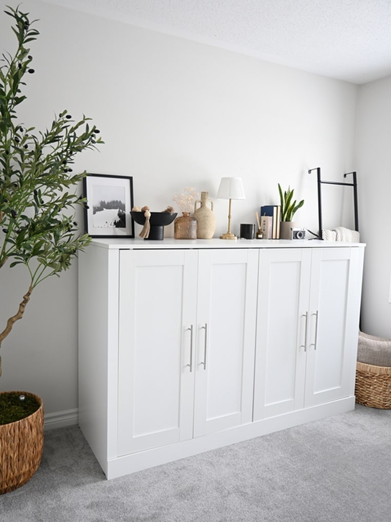 White Pur collection cabinet bed with decorative items in a room with a plant and basket.