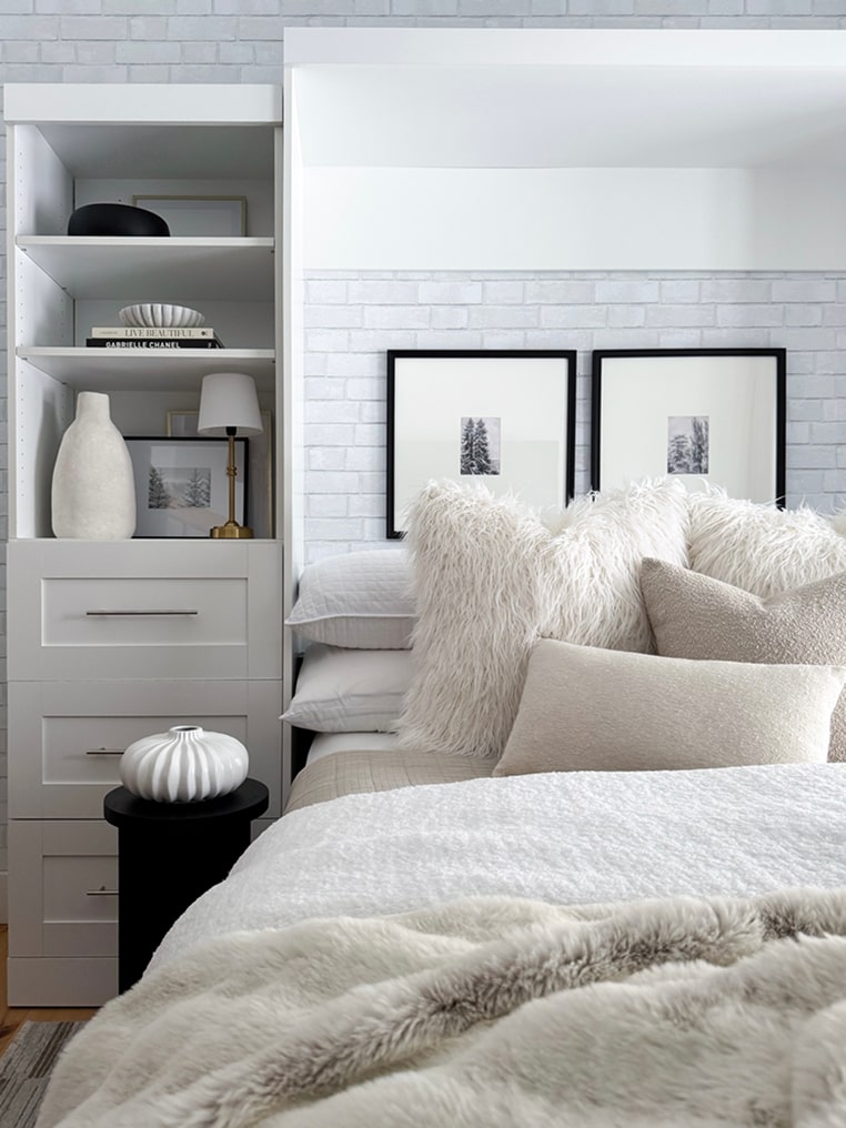 Neatly arranged bedroom with the Pur collection murphy bed, shelves, and framed pictures on a white brick wall.