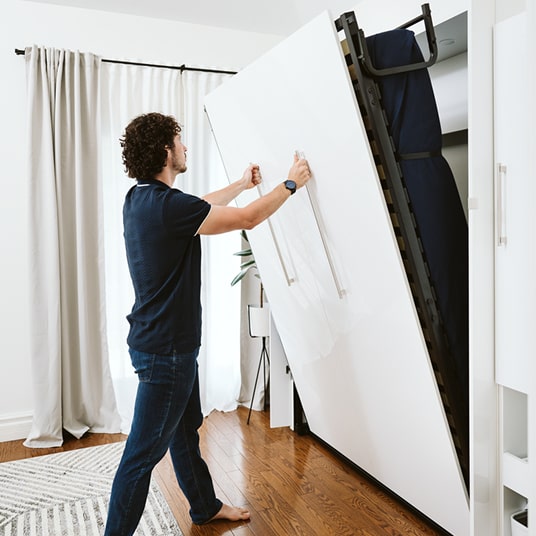 Man using a wall-mounted bed conversion system in a modern living room.
