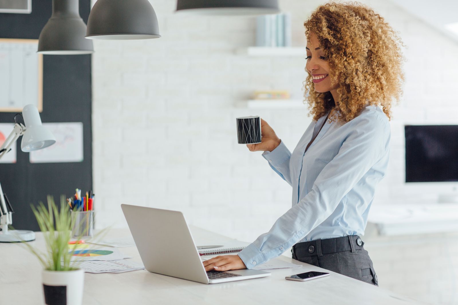 Businesswoman happily using her laptop and holding a mug