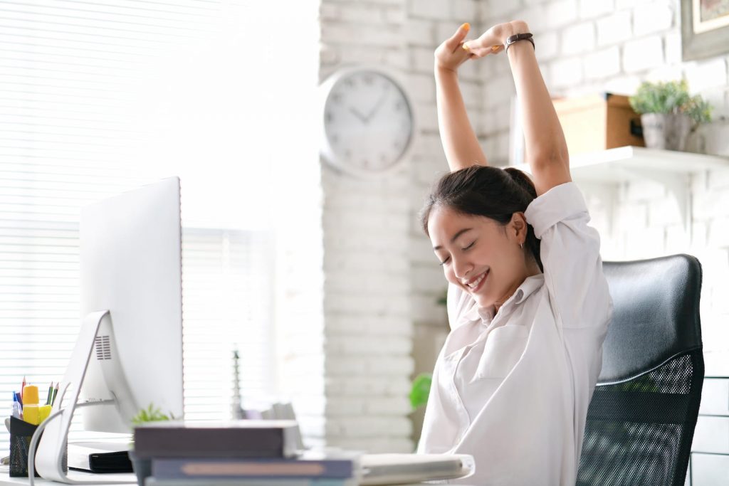 woman stretching with hand up in front of computer