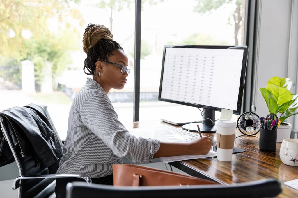 woman writing and working at computer next to big window