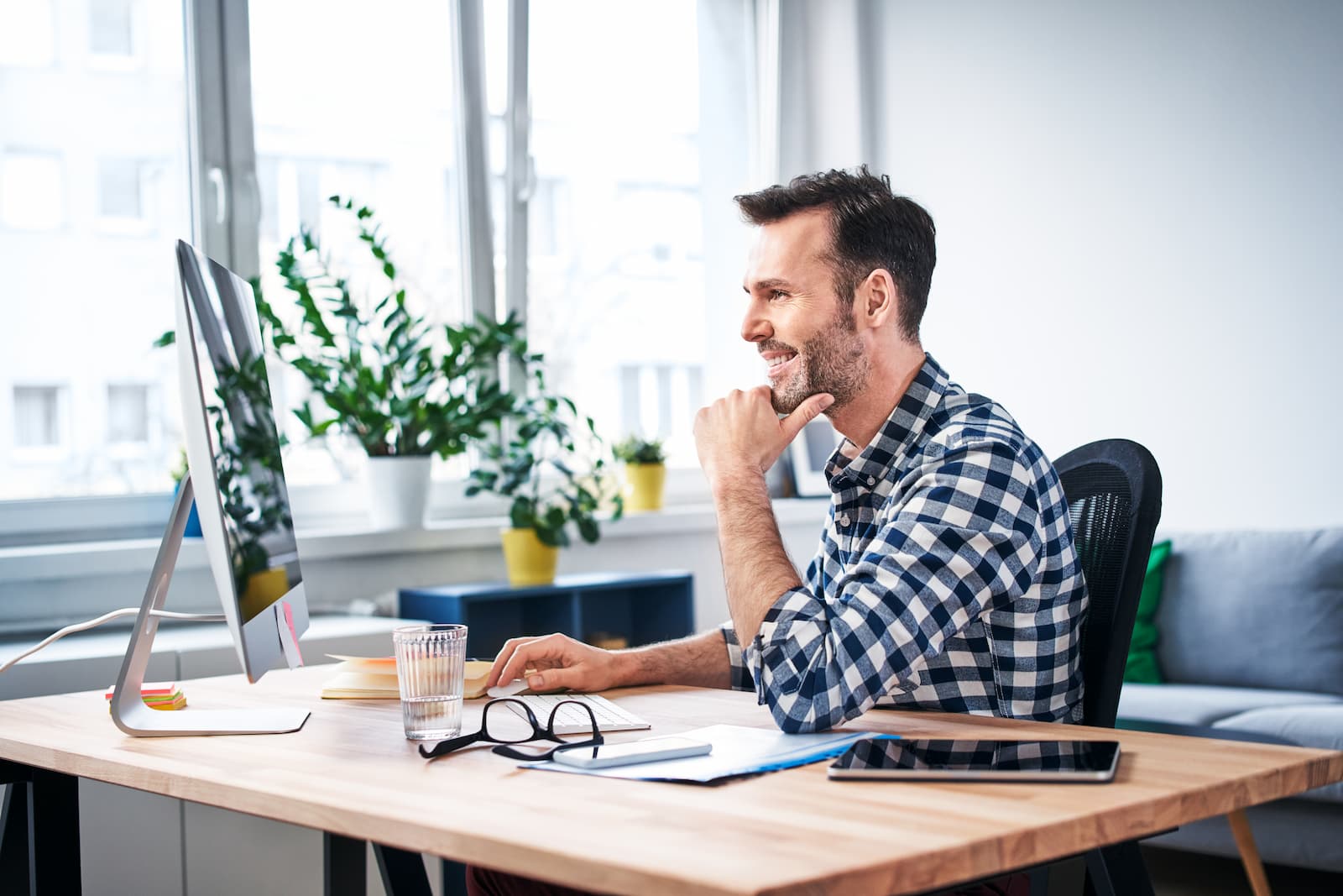 man sitting at a desk with computer smiling next to big open window