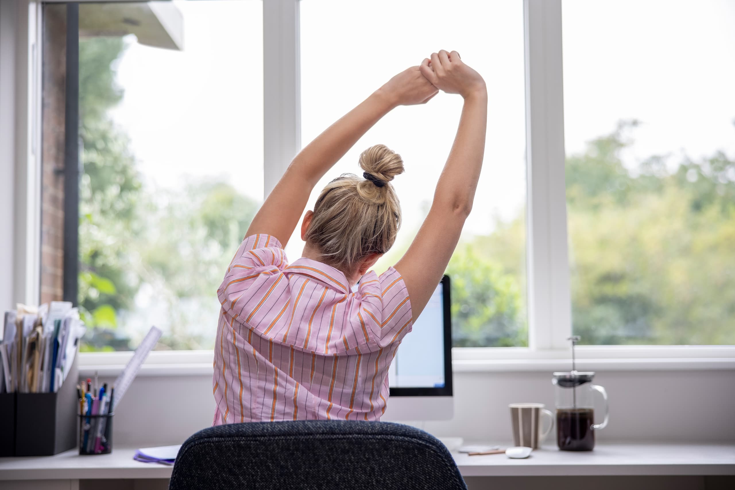 Woman stretching in her office in front of a window