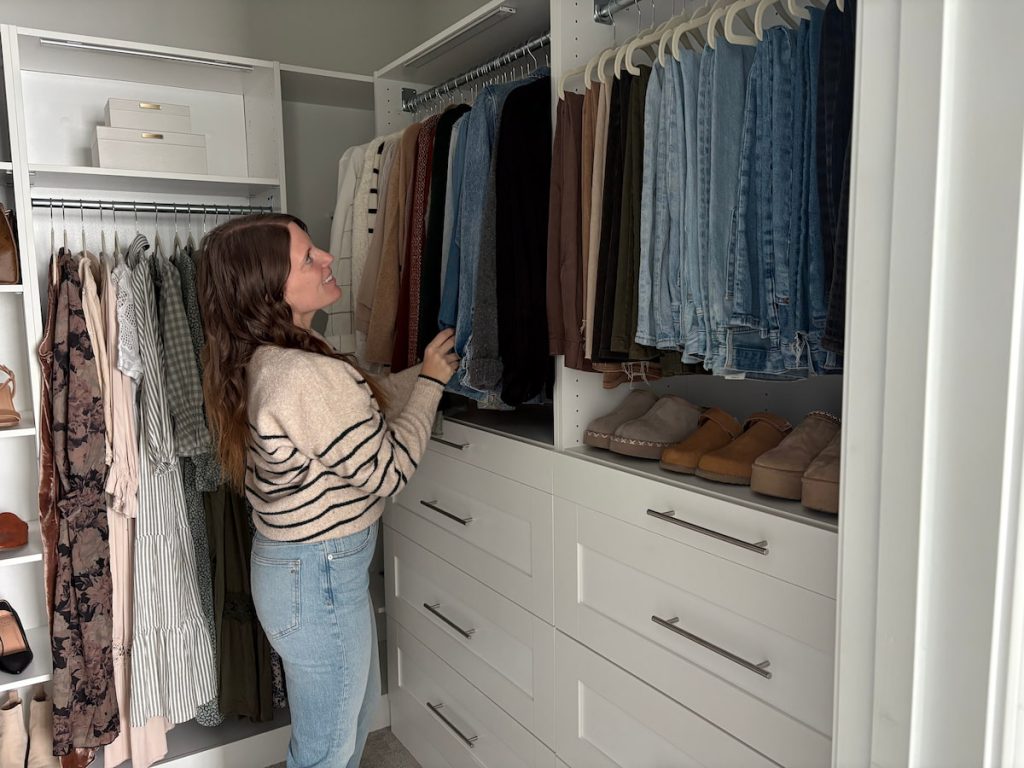 Woman organizing jeans on shelves inside a modular closet organizer with drawers and hangers